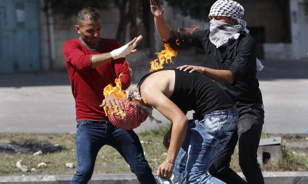 Manifestantes palestinos intentan apagar el fuego que quema a un compañero, originado por un cóctel molotov que él trataba de lanzar hacia las tropas israelíes durante los enfrentamientos en Hebrón, 13 de octubre de 2015. REUTERS / Mussa Qawasma