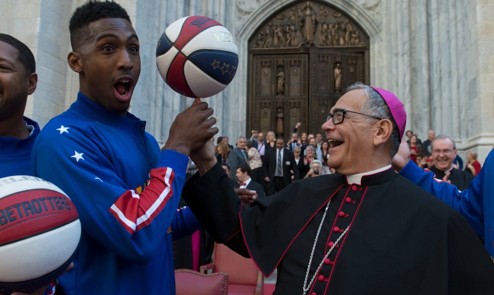 El Obispo Dominick Lagonegro gira una pelota de baloncesto en el dedo con la ayuda de los Harlem Globetrotters frente a la Catedral de San Patricio durante el desfile del día de Colón en la ciudad de Manhattan de Nueva York. REUTERS / Stephanie Keith