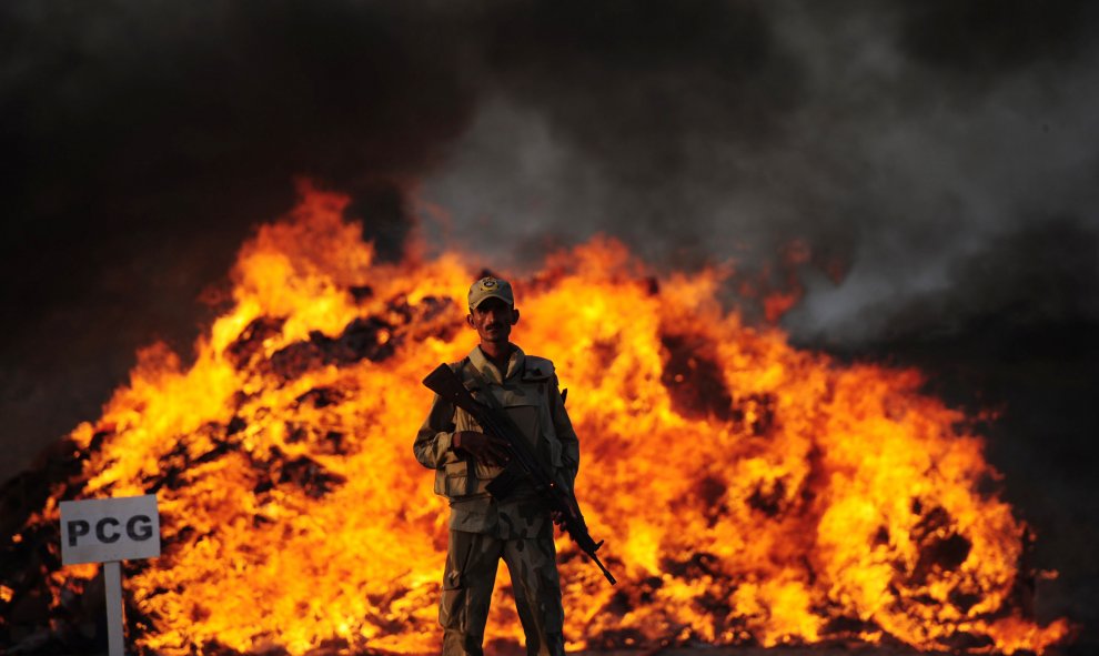 Un soldado paquistaní de la Fuerza contra Narcóticos se encuentra al lado de un montón de drogas en llamas que fueron incautadas en las afueras de Karachi, el 15 de octubre de 2015. AFP/ASIF HASSAN