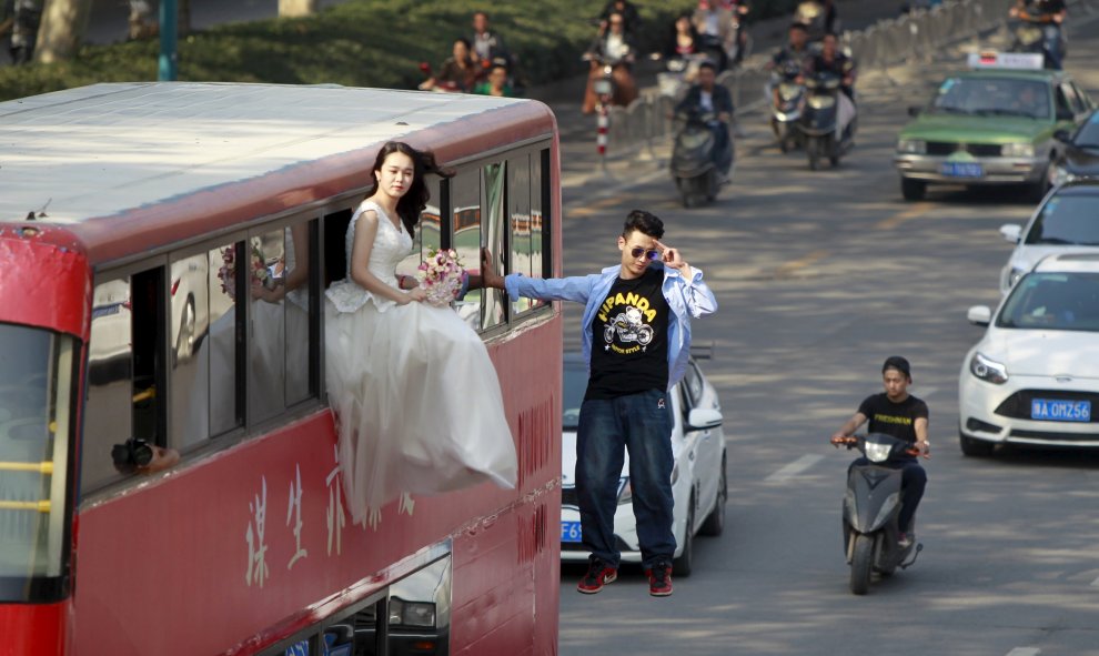 El mago Lei Xin es fotografiado colgado de un autobús , al lado de una mujer vestida de novia, mientras actúan en una calle de Zhengzhou, provincia de Henan, China. REUTERS / Stringer,