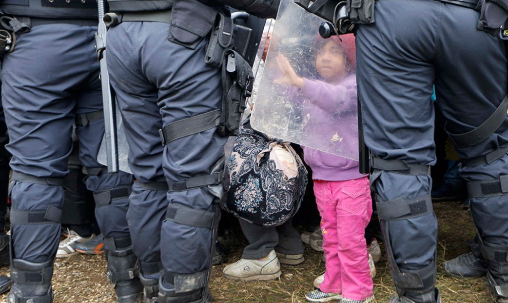 Una pequeña toca el escudo de un policía antidisturbios tras cruzar la frontera de Croacia, en Rigonce, Eslovenia.- SRDJAN ZIVULOVIC (REUTERS)