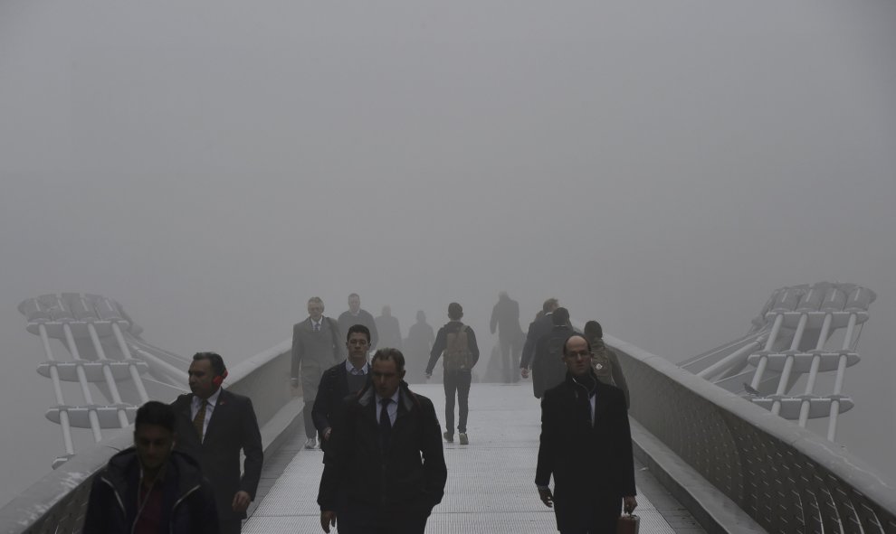 Trabajadores de la ciudad cruzan la pasarela del Milenio sobre el río Támesis entre la niebla.- REUTERS.