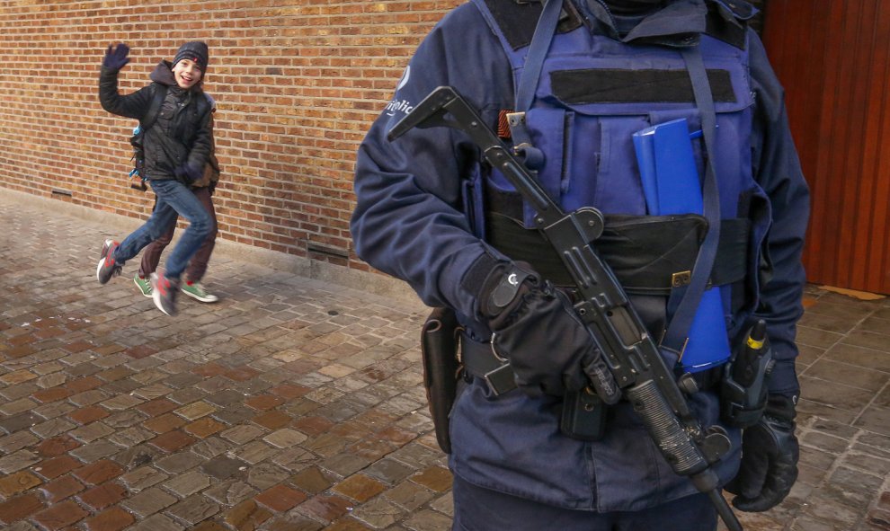 Dos niños saludan a la cámara con un salto detrás de un oficial de la policía belga que está de guardia a las afueras de una escuela en el centro de Bruselas, 25 de noviembre de 2015. REUTERS / Yves Herman