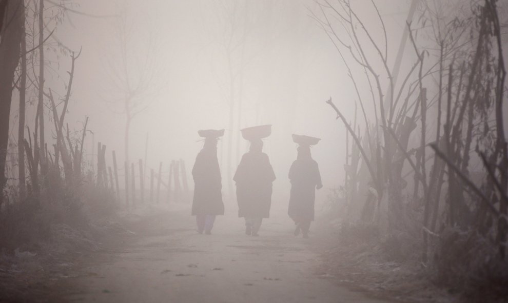 Mujeres Kashmiri portan cestas sobre sus cabezas mientras caminan entre una densa niebla a primera hora del día. Srinagar, India. REUTERS/Danish Ismail