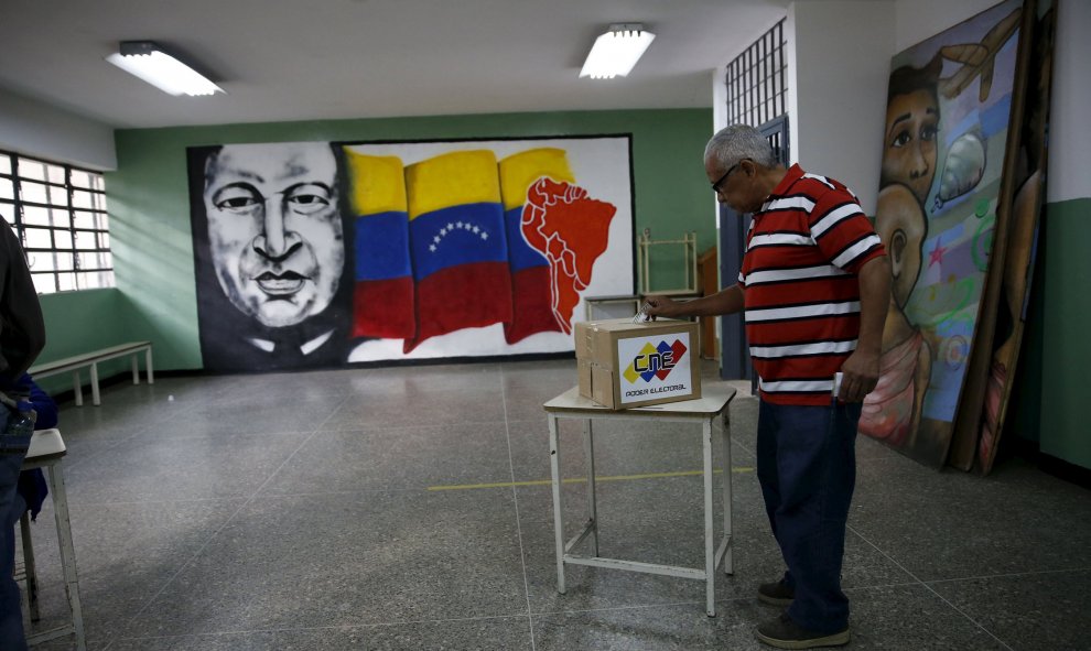 Un ciudadano venezolano deposita su voto con un mural de Chavez al fondo, en Caracas. REUTERS/Carlos Garcia Rawlins