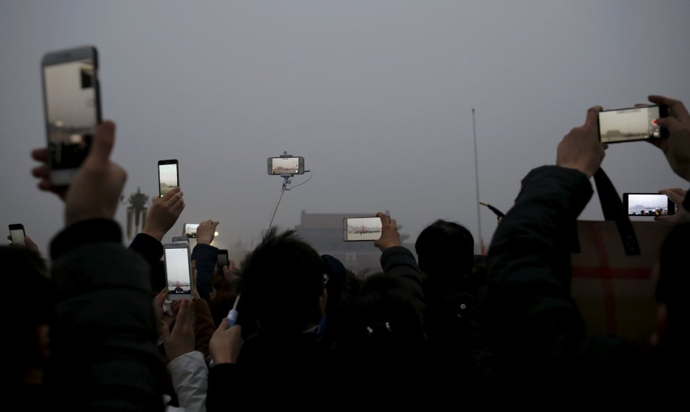 Gente graba durante la ceremonia de izada de bandera en medio de un fuerte humo en la Plaza de Tiananmen, tras activar la alerta roja por contaminación en Pekín. REUTERS/Damir Sagolj