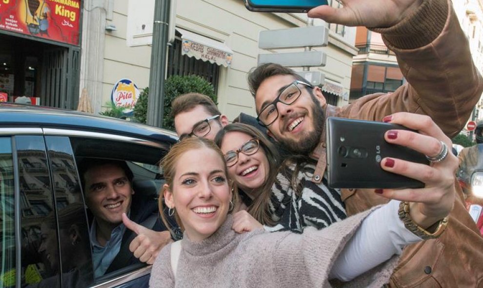 El presidente de Ciudadanos y candidato a la presidencia del Gobierno, Albert Rivera, dentro del coche se deja hacer un selfi con un grupo de jóvenes.- EFE