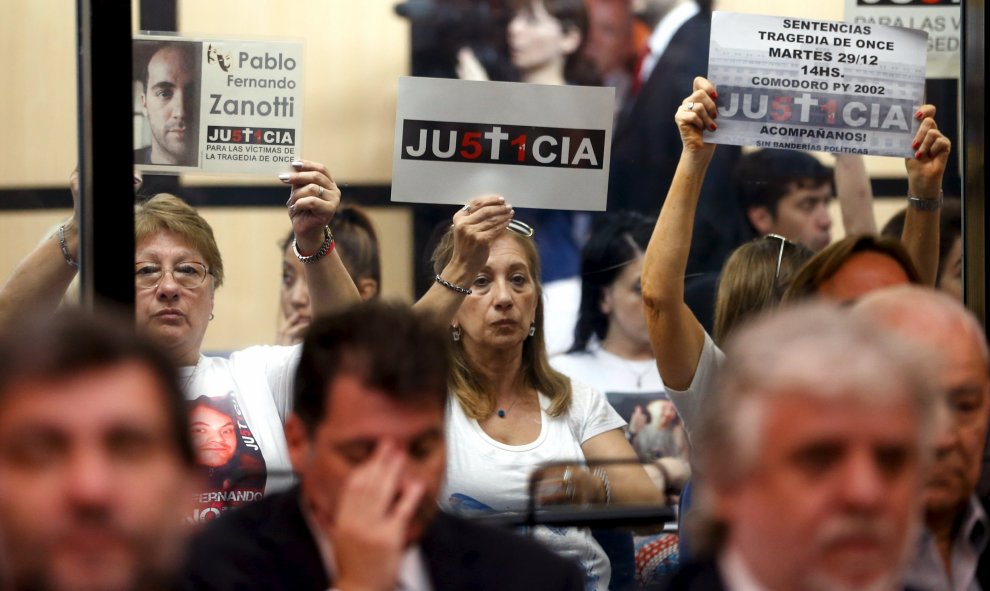 Los familiares de las víctimas de un accidente de tren en 2012 sostienen carteles que ponen "Justicia", sentados detrás de los acusados en una sala de audiencias en Buenos Aires, Argentina , 29 de diciembre de 2015. 51 personas murieron en el accidente y