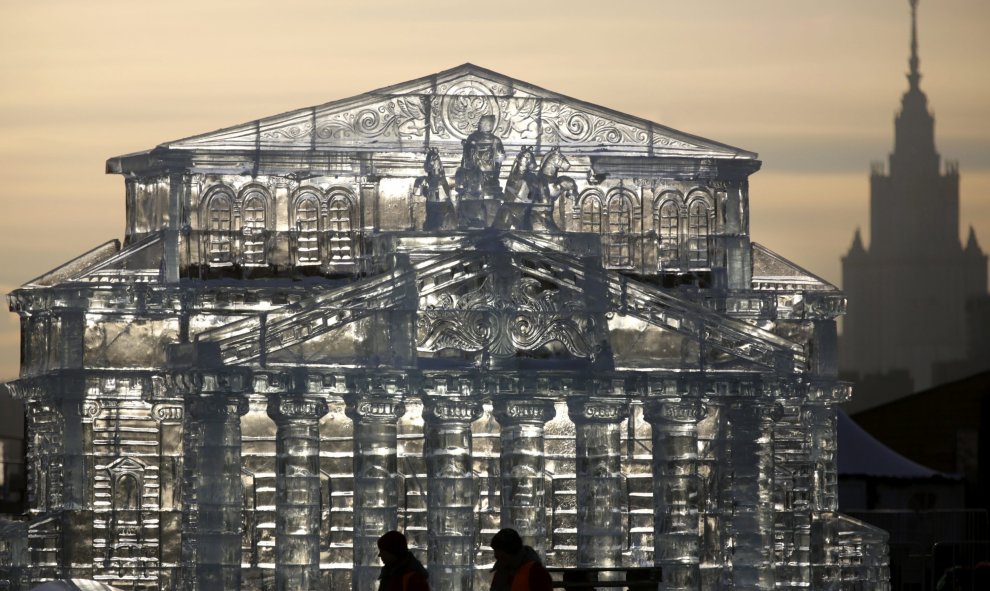 Dos artistas caminan junto a una escultura de hielo que representa el teatro Bólshoi en Moscú (Rusia) hoy, 29 de diciembre de 2015. Los moscovitas se preparan para las celebraciones de Año Nuevo el próximo 31 de diciembre, la Navidad según el calendario j