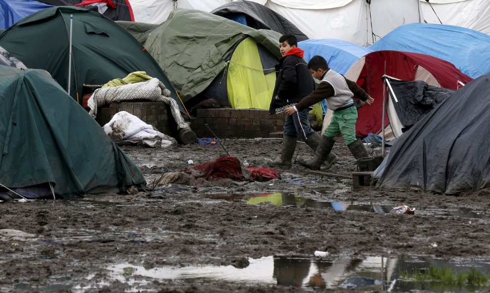 Dos niños inmigrantes caminan por el suelo enfangado entre las tiendas del  campamento provisional para refugiados de procedentes de Irak, Kurdistán, Irán y Siria, cerca de Dunkerque (Francia). REUTERS / Pascal Rossignol