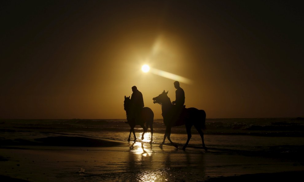 Unos palestinos pasean a caballo por la orilla de la playa en el atardecer de Gaza. REUTERS/Mohammed Salem