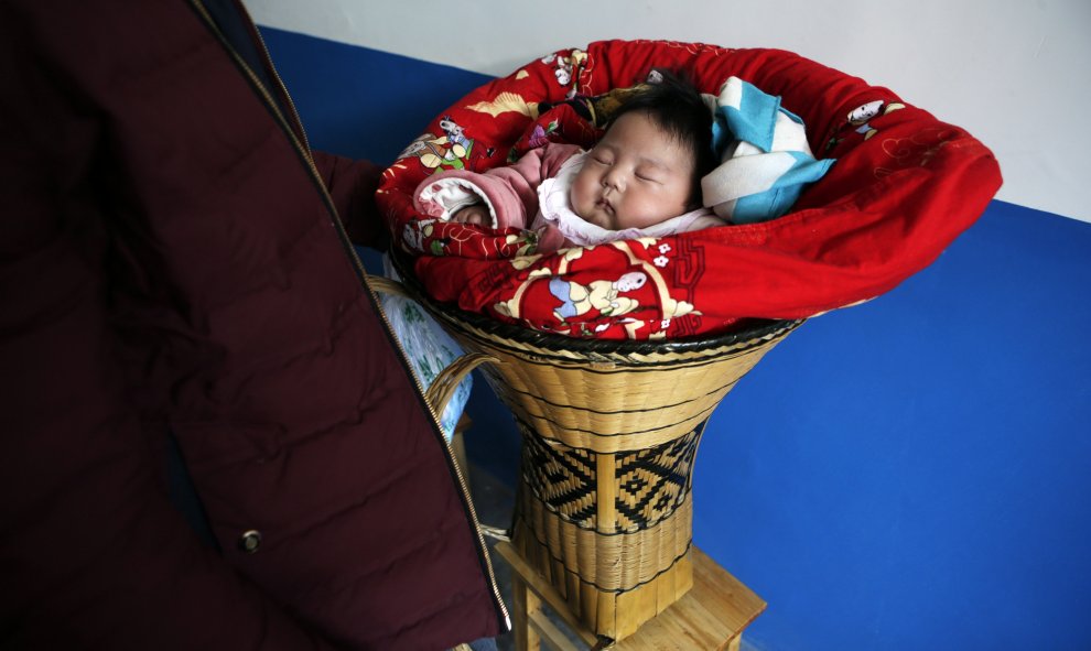 Una niña de 3 meses de edad se ve junto a su padre, envuelta en mantas en una cesta en una fiesta de bodas Tujia étnica tradicional durante se celebran el Año Nuevo Lunar en la ciudad Ziqiu, condado Changyang de la provincia china de Hubei, 15 de febrero