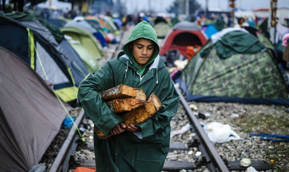 Un niño lleva leña bajo la lluvia en un campamento improvisado en la frontera entre Grecia y Macedonia, cerca de la localidad griega de Idomeni, donde miles de refugiados y migrantes están varados por el bloqueo de la frontera de los Balcanes. DIMITAR DIL