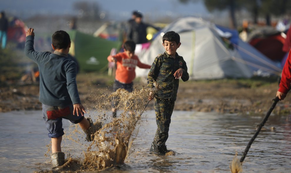 Niños migrantes juegan con el agua en un campamento improvisado inundado en la frontera entre Grecia y Macedonia, cerca de la localidad de Idomeni. REUTERS/Stoyan Nenov