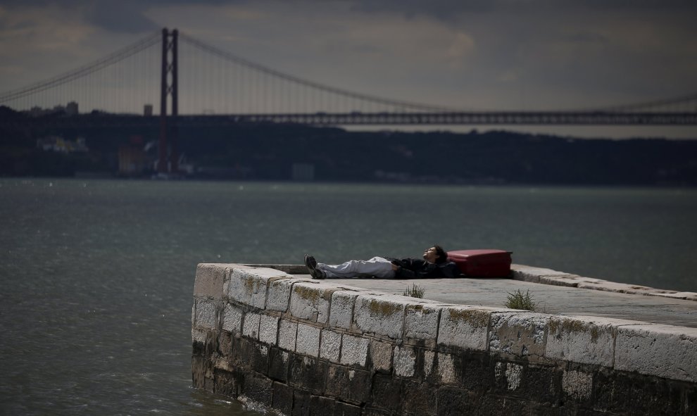Un hombre duerme en una barandilla en el río Tajo en el centro de Lisboa. REUTERS