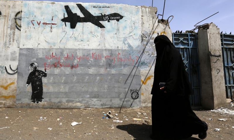 Una mujer camina junto a unas pintadas en contra de los drones estadounidenses y los ataques de Estados Unidos contra supuestas pociones de Al-Qaeda en Saná, Yemen. EFE/Yahya Arhab