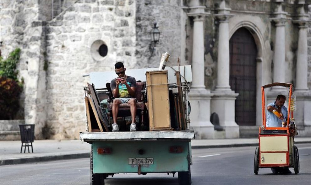 Un hombre juega con su teléfono móvil mientras viaja en la parte trasera de un camión en La Habana. EFE/Alejandro Ernesto