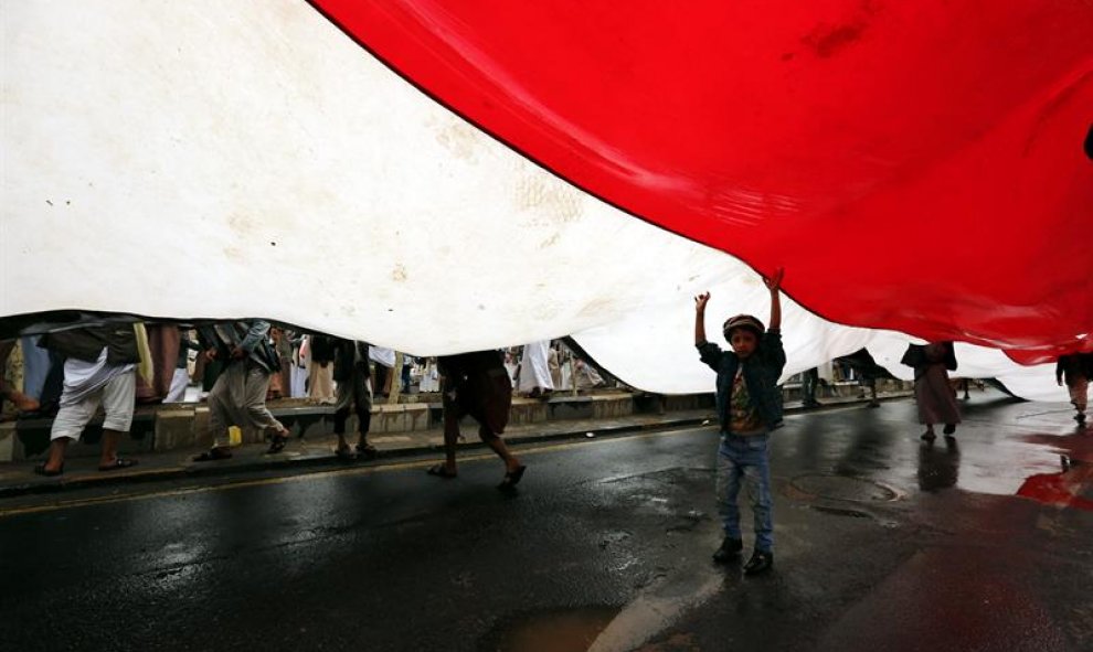 Cientos de personas llevan una bandera nacional durante una manifestación en contra de la violaciones al alto el fuego en Saná, Yeme. EFE/Yahya Arhab