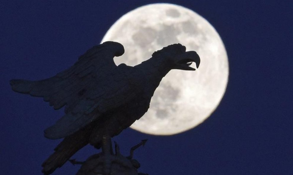 Una estatua con forma de águila en el castillo Sanssouci silueteada frente a la luna llena en Postdam, Alemania. EFE/Ralf Hirschberger