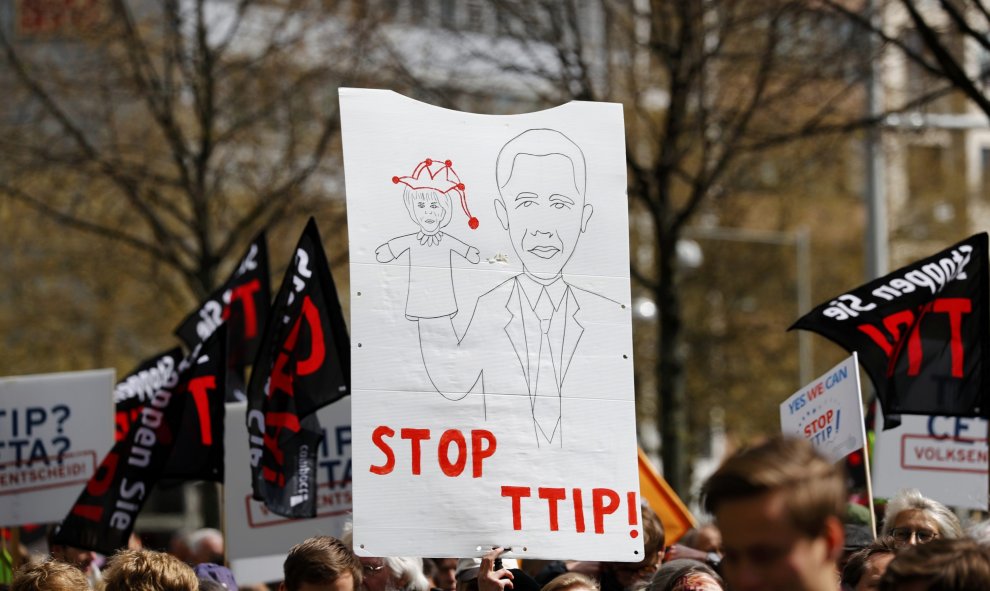 Pancarta con un dibujo de Obama, mientras sujeta a Merkel representada como una marioneta. REUTERS/Kai Pfaffenbach