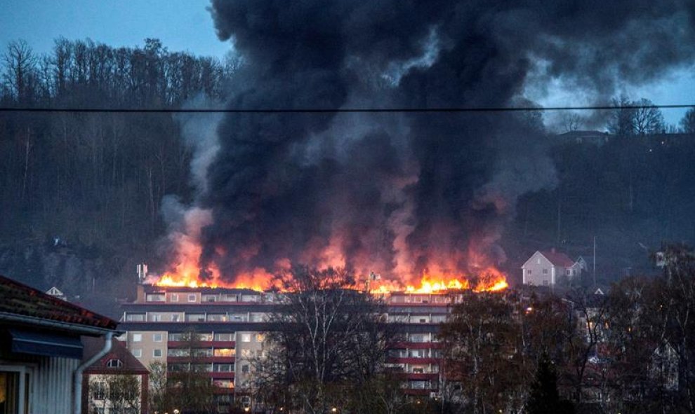 Varios bomberos intentan contener las llamas tras declararse un incendio en un complejo residencial en Huskvarna, en el sur de Suecia. El fuego se propagó rápidamente por el los áticos que obligó a 160 residentes a abandonar rápidamente sus viviendas. EFE