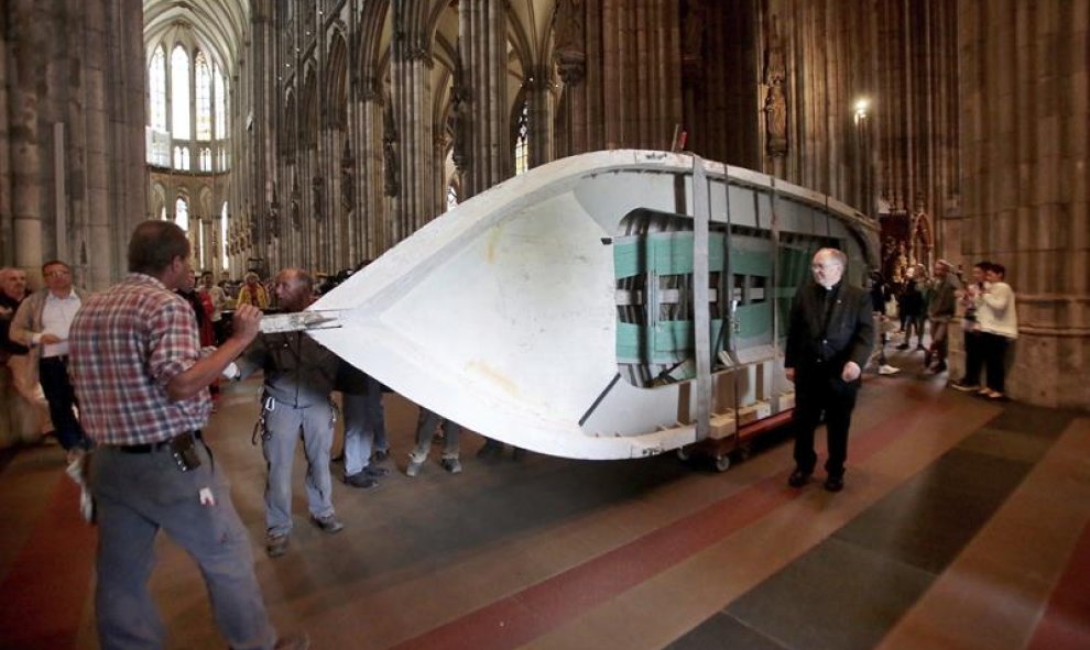 Varias personas trasladan una embarcación, que fue utilizada por refugiados, antes de colocarla para su exhibición en la catedral de Colonia, Alemania. EFE/Oliver Berg