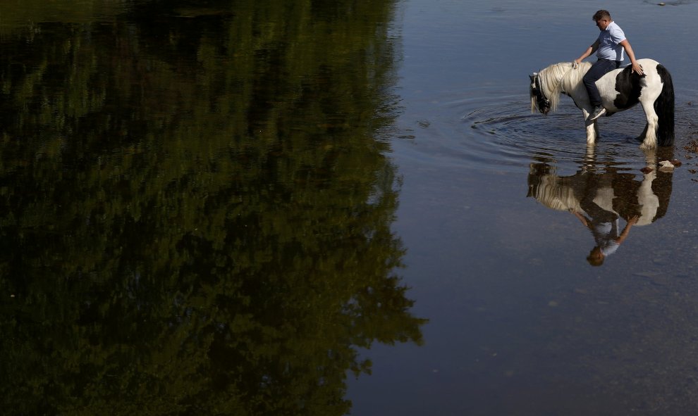 Un miembro de la 'comunidad de los viajeros' da de beber a su caballo en el río Eden, al norte de Britain. REUTERS/Phil Noble