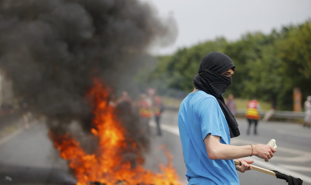 Un manifestante enmascarado junto a neumáticos en llamas que bloquean la carretera durante las protestas contra la ley la reforma laboral en Nantes, Francia. REUTERS/Stephane Mahe