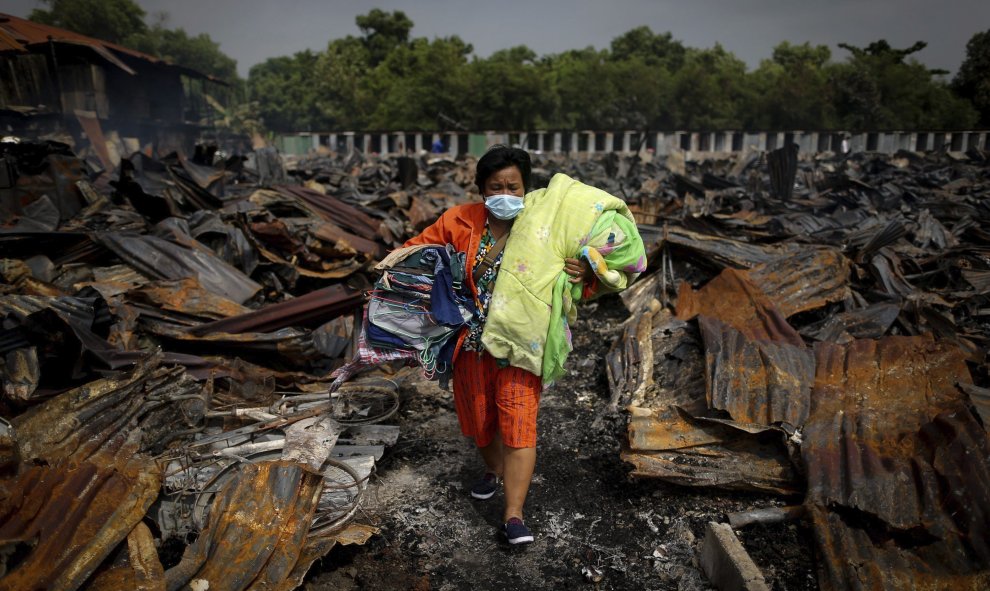 Una mujer carga con los objetos personales que han podido rescatar de los restos de su casa tras el incendio declarado anoche en el distrito Don Muang de Bangkok, Tailandia. EFE/Diego Azubel