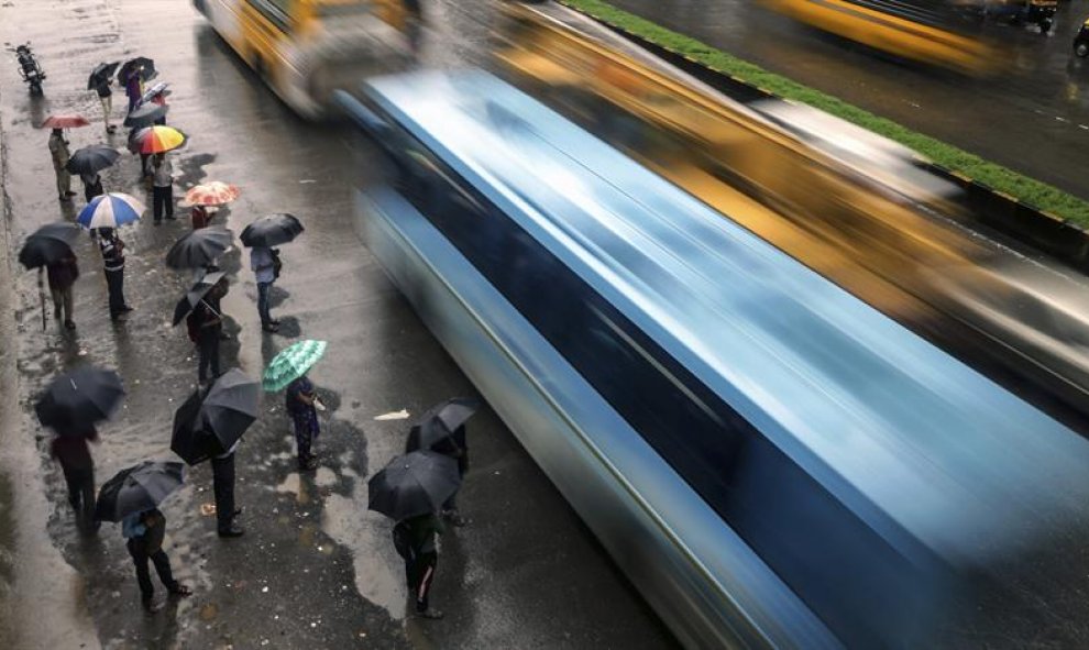 Un grupo de personas se protege de la lluvia en Bombay, India. Al menos 24 personas han muerto y 9 se encuentran desaparecidas por las fuertes lluvias caídas en los últimos días en el estado central indio de Madhya Pradesh.  EFE/Divyakant Solanki.