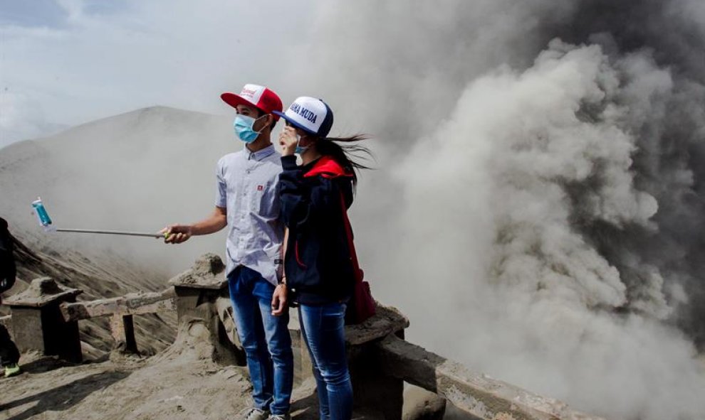 Dos jóvenes posan para un selfie mientras el volcán Bromo arroja cenizas al aire durante una erupción volcánica en Probolinggo, Indonesia. EFE/Fully Handoko