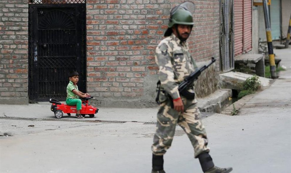 Un niño indio juega con su coche mientras un solado monta guardia durante el toque de queda en Srinagar después de las protestas por lamuerte un insurgente separatista hace 14 días/EFE