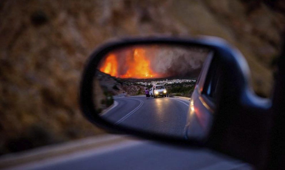 Fotografía que muestra a unas personas mientras observan una densa nube de humo sobre el pueblo de Lithi, durante un incendio forestal en la isla de Quíos, Grecia. Las llamas han quemado 3.500 hectáreas de terreno forestal y agrícola, aunque ya se encuent