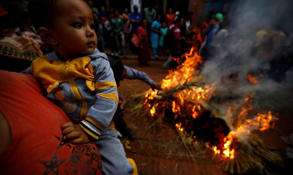 Una mujer lleva a un niño mientras arde una efigie del demonio Ghantakarna para simbolizar la destrucción del mal, durante el festival Ghantakarna en la antigua ciudad de Bhaktapur. REUTERS/Navesh Chitrakar