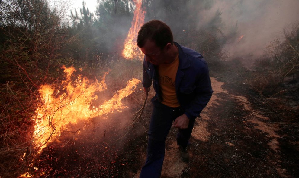 Han sido muchos voluntarios los que han ayudado a la extinción de los fuegos, en esta fotografía un hombre de Arbo, observa el fuego con una rama/REUTERS