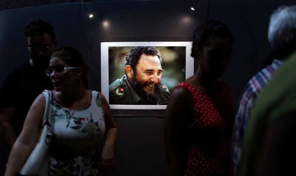 Varias personas junto a uno de los retratos del líder de la revolución cubana, Fidel Castro, que forman parte de la exposición 'Fidel', con motivo de su 90 cumpleaños. REUTERS/Alexandre Meneghini