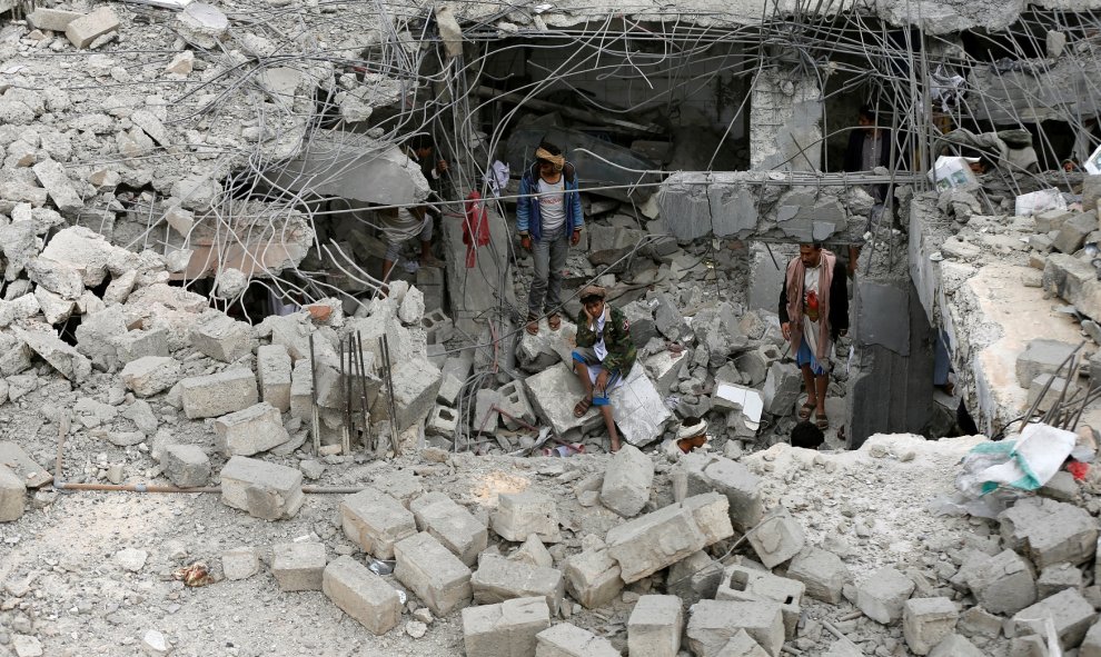 Un hombre permanece sentado junto a otros entre los escombros de un edificio derruido por los ataques aéreos saudíes en Amran, Yemen. REUTERS/Khaled Abdullah