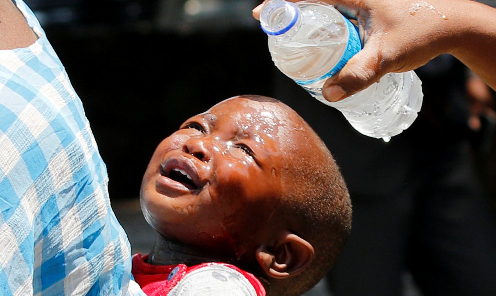 Una mujer vierte agua sobre la cabeza de un niño afectado por los gases lacrimógenos después de los enfrentamientos entre la policía y los vendedores ambulantes en el centro de Harare, Zimbabue. REUTERS/Philimon Bulawayo