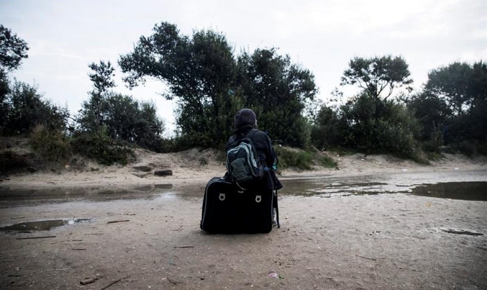 Un inmigrante espera junto a su equipaje en el campamento conocido como la 'Jungla' durante su desmantelamiento en Calais, Francia. EFE/Etienne Laurent