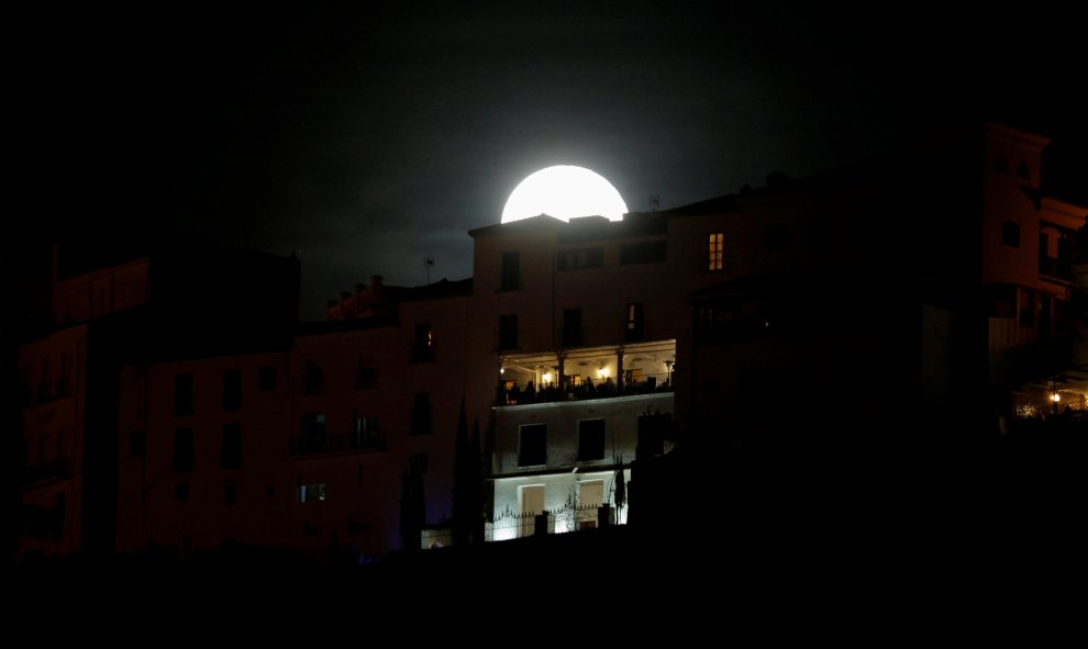 Un grupo de personas se asoma a un balcón mientras la Superluna se alza tras ellos en Ronda. REUTERS/Jon Nazca