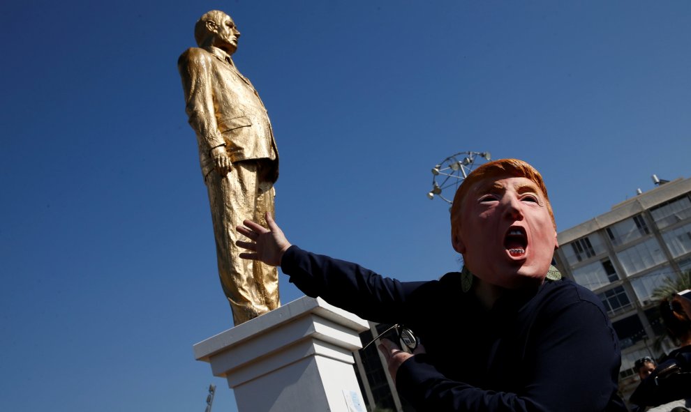 Una persona con una máscara de Donald Trump, junto a la estatua del primer ministro de Israel Benjamin Netanyahu, antes de ser derruida. REUTERS/Baz Ratne