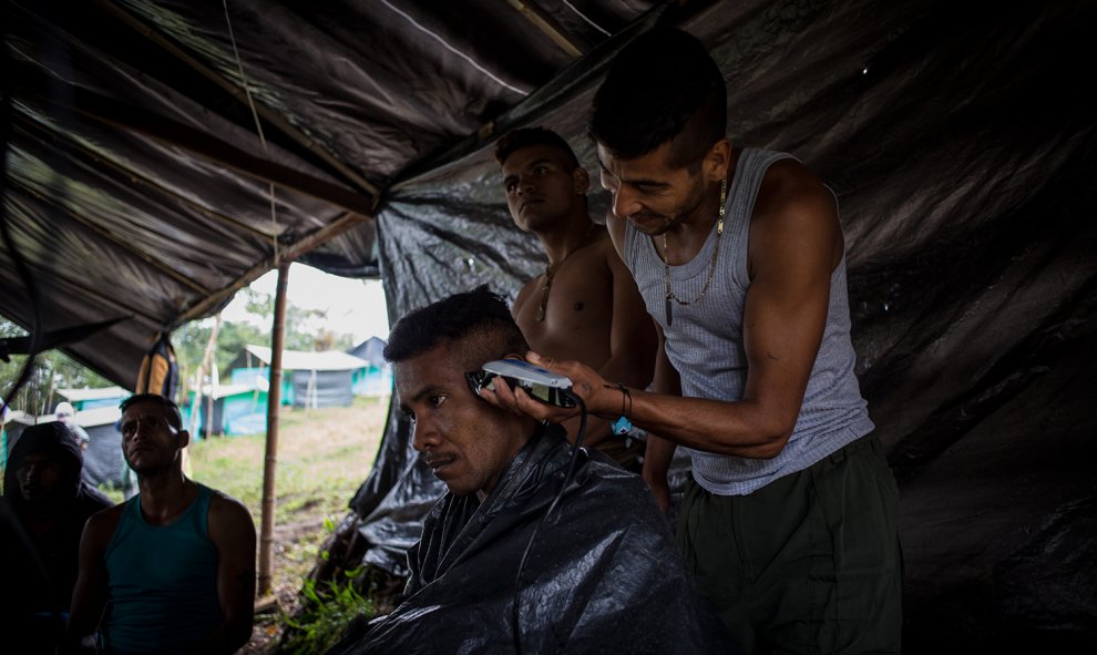 Un guerrillero le corta el pelo a otro mientras el resto ve una película en una carpa del campamento de desmobilizados de las FARC de La Fila, en la región de Tolima.- JAIRO VARGAS