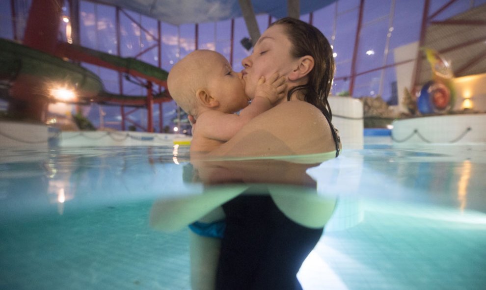 Una madre finlandesa besa a su bebé durante una clase de natación. AFP