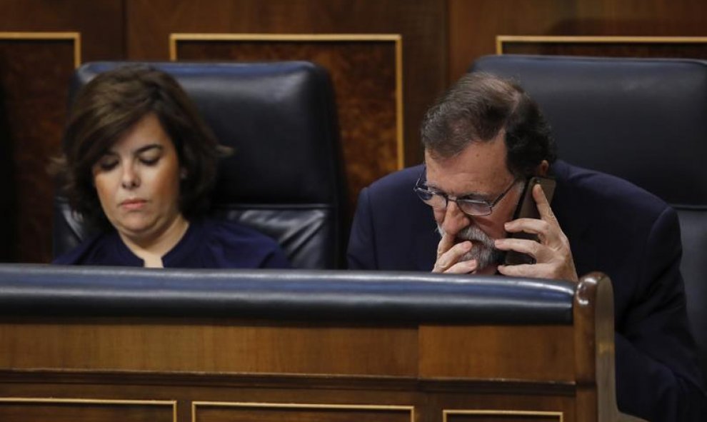 Rajoy hablando por teléfono mientras interviene la portavoz de Podemos. EFE