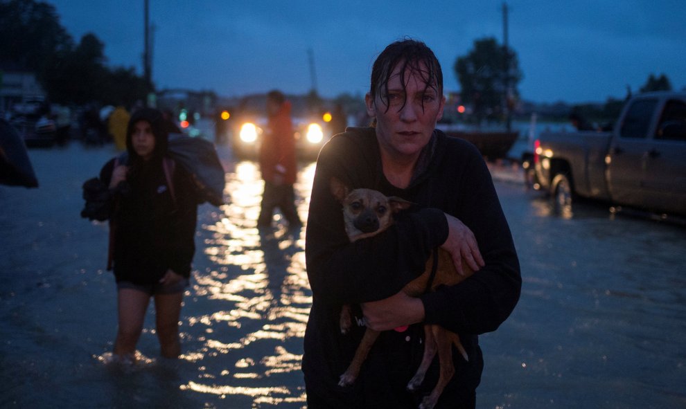 Una mujer lleva a su  perro en brazos tras ser evacuada de su casa debido a las inundaciones causadas por la tormenta tropical Harvey, en Houston, Texas (EEUU).- REUTERS