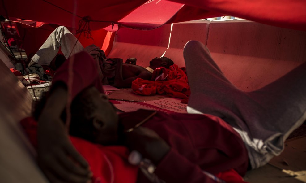 Dos migrantes se protegen del sol bajo una manta en el puerto del Algeciras. Han pasado varias noches allí debido al colapso en los polideportivos y dependencias policiales tras llegar en patera a España. JAIRO VARGAS