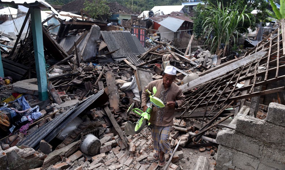 Un hombre lleva una bicicleta y atraviesa las ruinas de las casas dañadas por el terremoto que ha sacudido el oeste de Lombok, Indonesia. / Reuters