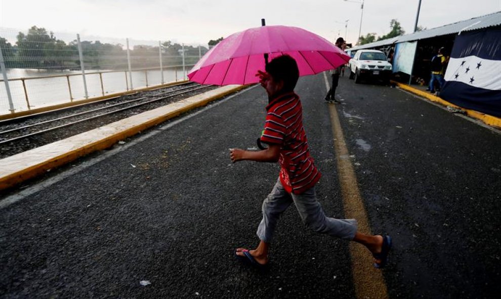 Alex corre bajo la lluvia en el puente de la frontera entre Guatemala y México. EFE/ESTEBAN BIBA