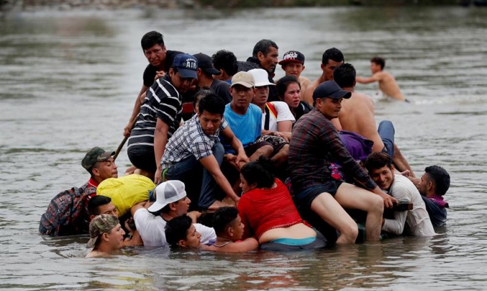 Decenas de migrantes hondureños cruzan a pie y el balsa el río Suchiate, que separa a Guatemala de México, mientras otros observan desde un puente. EFE/Esteban Biba