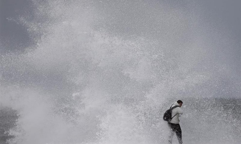 Un ciudadano desafía el fuerte oleaje en la playa de Barceloneta, durante el temporal marítimo que afecta a toda la costa catalana. EFE/ Andreu Dalmau